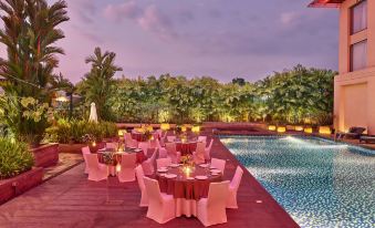 an outdoor dining area with a pool in the background , surrounded by lush greenery and trees at Courtyard Kochi Airport