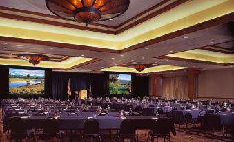 a large conference room with rows of tables and chairs , multiple screens , and a flag in the background at Sunriver Resort
