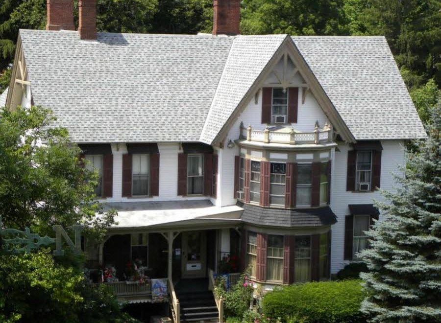 a large , two - story house with a porch and red shutters , surrounded by lush greenery and trees at Black Swan Inn