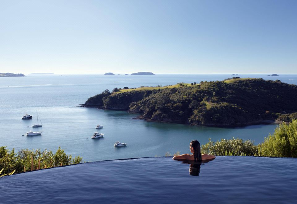 a woman is relaxing in a swimming pool , surrounded by a beautiful view of the ocean and mountains at Delamore Lodge
