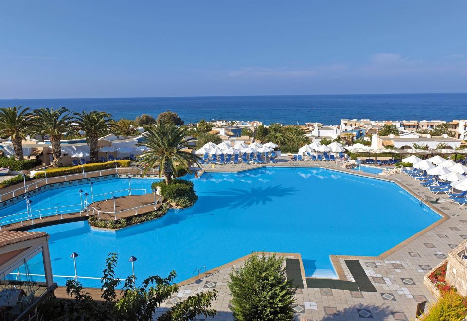 a large , blue swimming pool surrounded by lush greenery and a view of the ocean at Aldemar Knossos Royal