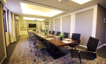 a conference room with a long wooden table , multiple chairs , and a television mounted on the wall at Brittany Hotel Global South Formerly Mella Hotel