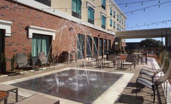 an outdoor courtyard with a fountain , lounge chairs , and tables , surrounded by a brick building at Courtyard LaGrange