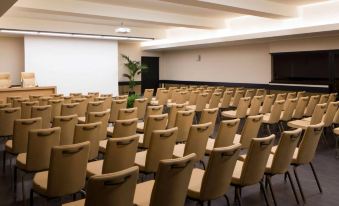 a conference room with rows of chairs arranged in a semicircle , and a projector screen on the wall at Hotel Mediterraneo