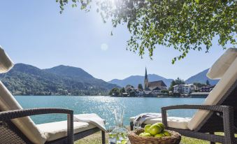 a serene lake scene with a mountain in the background and two chairs on the shore at Althoff Seehotel Uberfahrt