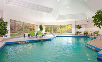 an indoor swimming pool with a green lounge area , surrounded by chairs and tables for relaxation at Holiday Inn Laval - Montreal