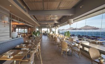 a large , well - lit restaurant with wooden floors and tables set for dining , overlooking the ocean at Condado Vanderbilt Hotel