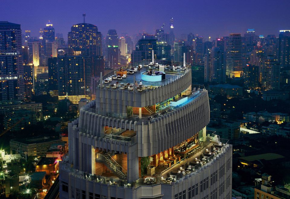 A cityscape at night showcases a skyline adorned with various buildings, including one resembling a castle, illuminated by the ambient glow of streetlights and windows, resulting in a captivating and picturesque scene at Bangkok Marriott Hotel Sukhumvit