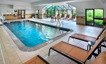 an indoor swimming pool surrounded by lounge chairs , with several people enjoying their time in the pool area at Courtyard Lincroft Red Bank