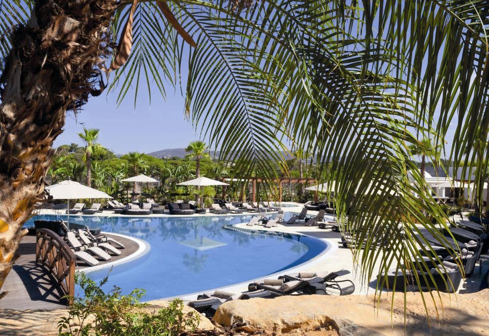 a resort with a large pool surrounded by lounge chairs and umbrellas , as well as palm trees in the background at Conrad Algarve