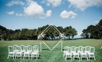 a wedding ceremony taking place in a grassy field , with a white arch and chairs set up for guests at Ardeena