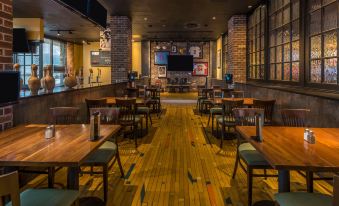 a dimly lit restaurant with wooden tables and chairs , a bar area , and a television at Four Points by Sheraton Juneau