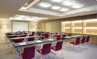 a large conference room with rows of chairs arranged in a semicircle , and a projector on the wall at Barcelo Hotel Oviedo Cervantes