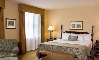 a hotel room with a king - sized bed , a chair , and a window overlooking a city street at The Saint Paul Hotel