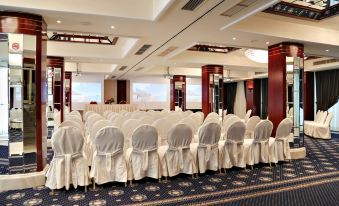 a large , empty conference room with rows of white chairs and a blue carpeted floor at Mediterranean Hotel