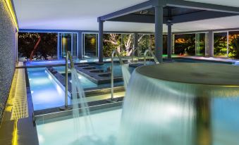 an indoor swimming pool with a waterfall feature , surrounded by trees and lit up at night at Chateau Royal Beach Resort & Spa, Noumea