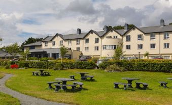 a large , yellow building with a green roof is surrounded by a well - maintained lawn and picnic tables at Arklow Bay Hotel