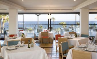 a restaurant with white tablecloths , wooden chairs , and tables set for dining , overlooking the ocean at Parador de Mojacar