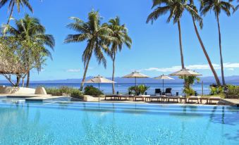 a beautiful swimming pool with palm trees and umbrellas , set against a backdrop of the ocean at Jean-Michel Cousteau Resort Fiji