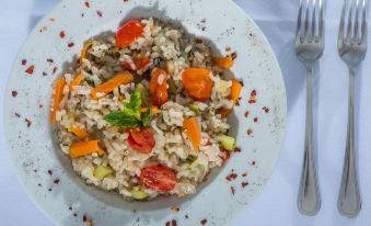 a white plate with a bowl of rice topped with meat and vegetables , accompanied by a fork at Naxos Palace Hotel