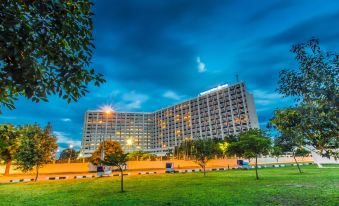 a tall building with a modern design is lit up at night , surrounded by green grass and trees at Transcorp Hilton Abuja