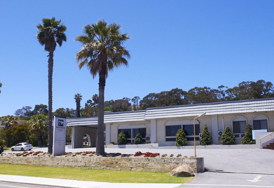 a white building with palm trees in front of it and a sign on the left at Dog Rock Motel