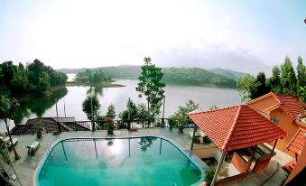 a large swimming pool with a red tile roof and trees surrounding it , overlooking a lake at Phong Nha Lake House Resort