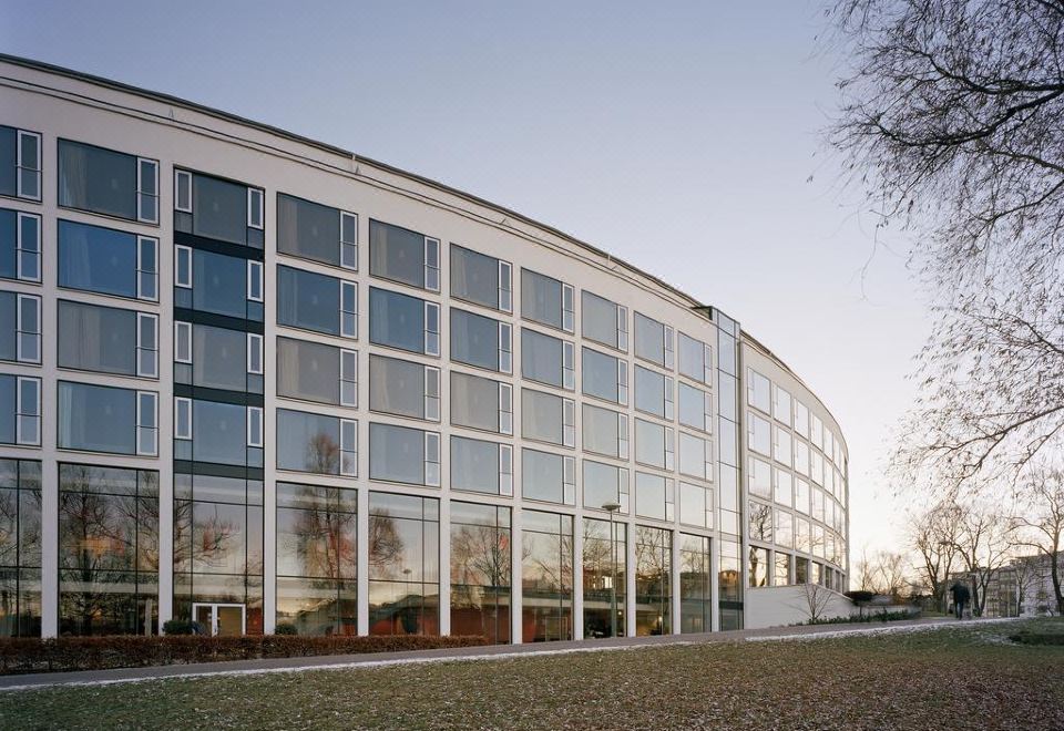a modern building with a curved facade and large windows is shown in the evening at Scandic Linkoping City