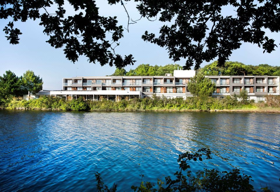 a large hotel situated on the edge of a body of water , surrounded by trees and grass at Best Western Plus Hotel les Rives du Ter