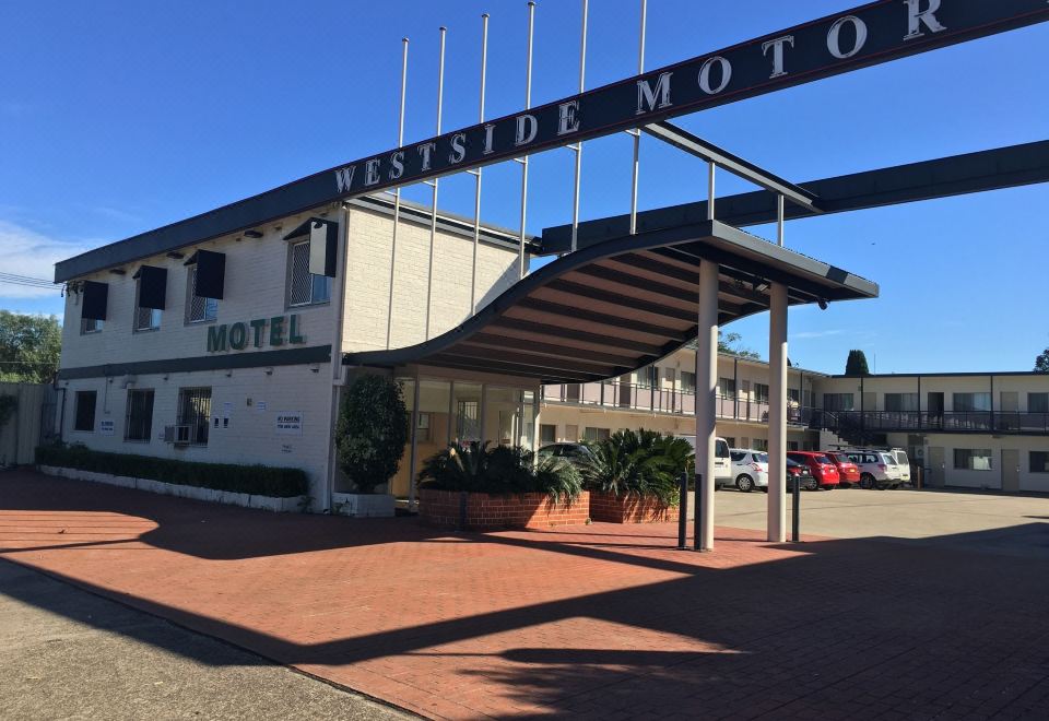 a modern hotel with a large sign above the entrance , and cars parked in front of the building at Westside Motor Inn