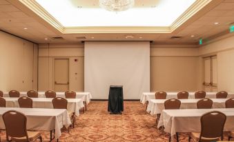 a conference room with rows of chairs and tables , a projector screen , and a chandelier at General Morgan Inn