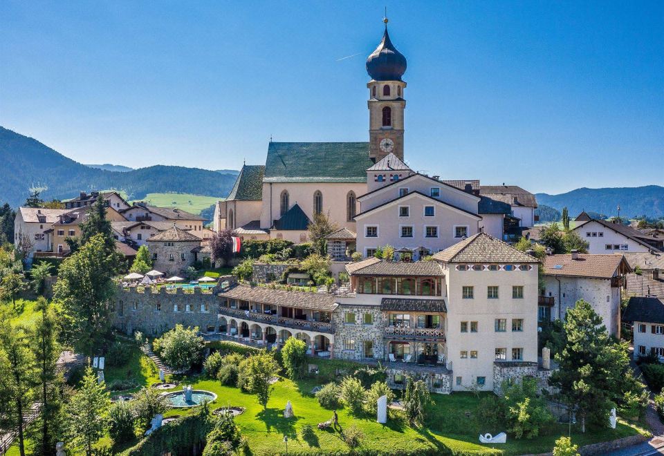 a beautiful church with a tall bell tower , surrounded by lush green trees and mountains in the background at Romantik Hotel Turm