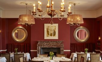 a dining room with a large chandelier hanging above a table , surrounded by chairs and a fireplace at Ockenden Manor Hotel & Spa