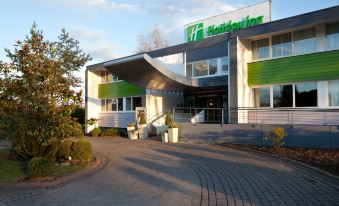 "a large white building with a green sign that says "" holiday inn "" is surrounded by a brick walkway" at Holiday Inn Lille - Ouest Englos