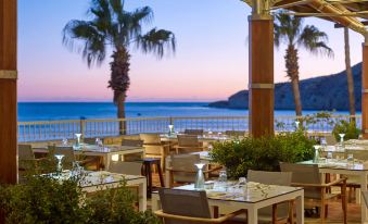 a restaurant with outdoor dining tables and chairs , overlooking the ocean at sunset , creating a serene atmosphere at Columbia Beach Resort