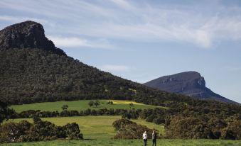 a couple of people are walking on a grassy hill with trees and mountains in the background at Royal Mail Hotel