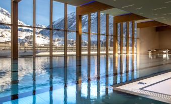 an indoor swimming pool surrounded by large windows , allowing natural light to illuminate the space at Radisson Blu Hotel Reussen Andermatt