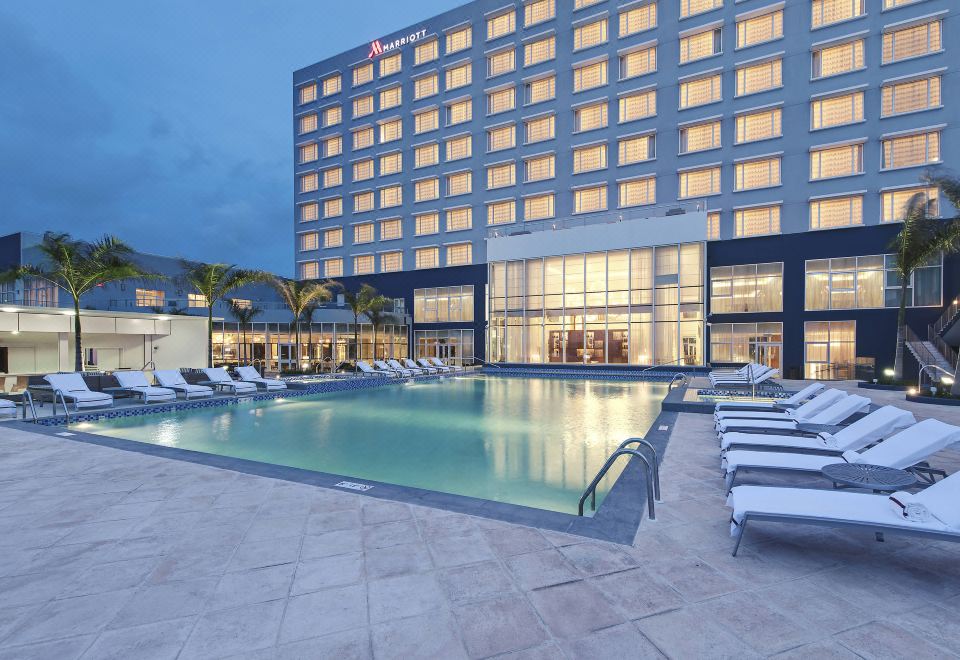 a large hotel with a swimming pool and lounge chairs is shown at dusk at Guyana Marriott Hotel Georgetown
