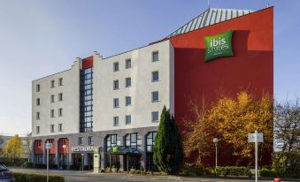 a large hotel with a red and white facade , surrounded by trees and a clear blue sky at Ibis Styles Lille Marcq-en-Baroeul