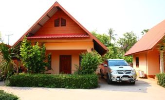 a red - roofed house with green shrubs and trees surrounding it , with a white car parked in front of it at Baan Rim Khong Resort