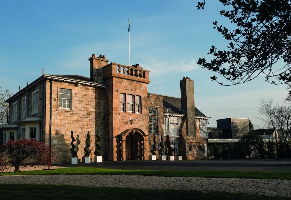 a large , red brick building with a flagpole and arched entrance , surrounded by trees and grass at Dalmeny Park House Hotel