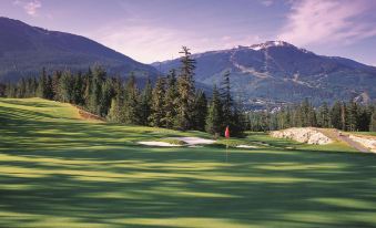 a golf course with green grass , trees , and mountains in the background , under a clear blue sky at Fairmont Chateau Whistler