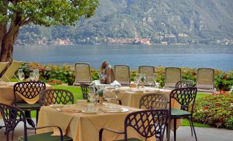 an outdoor dining area with tables and chairs set up near a body of water at Grand Hotel Menaggio