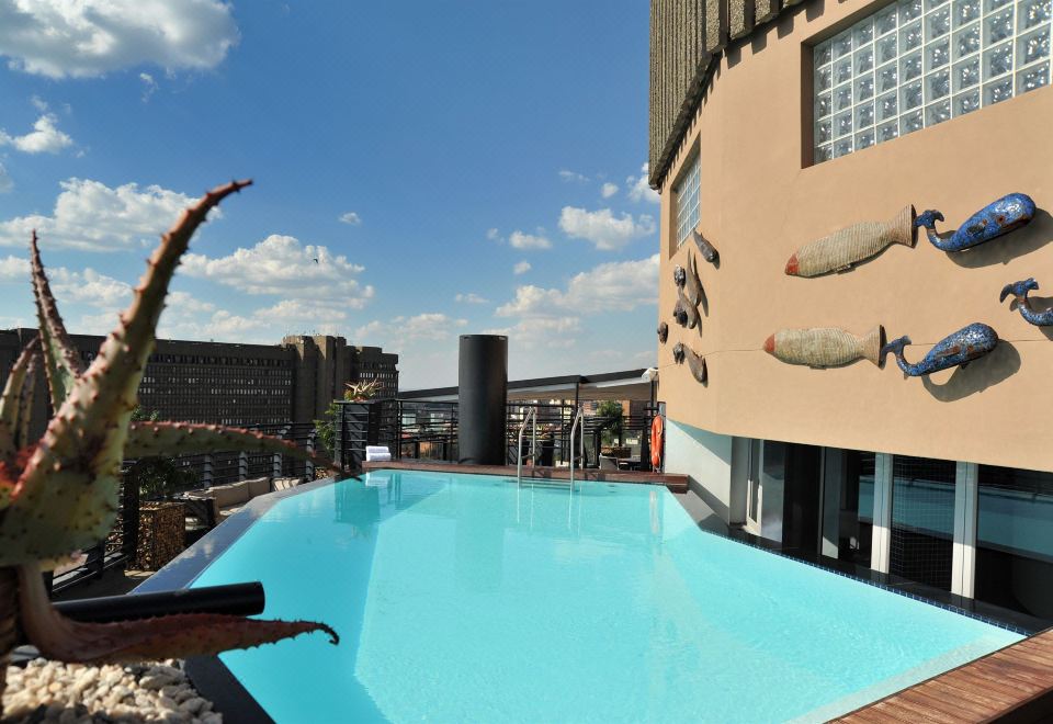 There is a swimming pool in front of the building with an outdoor view, and there is also a large white house located behind it at Anew Hotel Parktonian Johannesburg