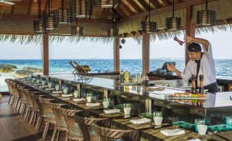 a wooden bar with a thatched roof , surrounded by palm trees and overlooking the ocean at Kurumba Maldives