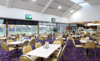 a large , well - lit room with multiple tables and chairs , and a television mounted on the wall at Thurgoona Country Club Resort