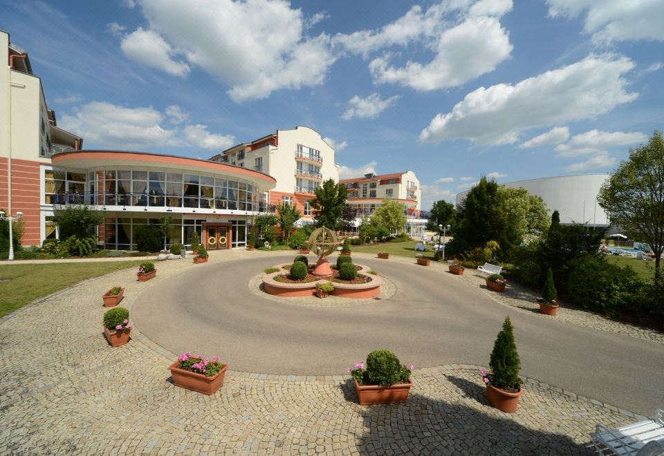 a large building with a circular driveway and flower beds in front of it , under a partly cloudy sky at The Monarch Hotel