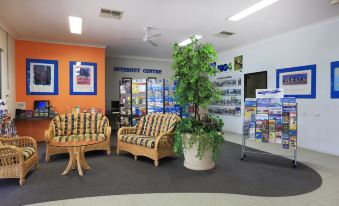 a cozy living room with comfortable furniture , including two couches and a coffee table , surrounded by posters and a large potted plant at Discovery Parks - Perth Airport