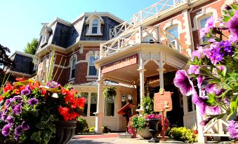 a large red brick building with a white porch , surrounded by lush greenery and colorful flowers at Prince of Wales