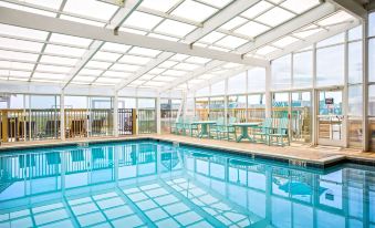 a large indoor swimming pool surrounded by glass walls , with people enjoying their time in the pool area at Ramada Plaza by Wyndham Nags Head Oceanfront